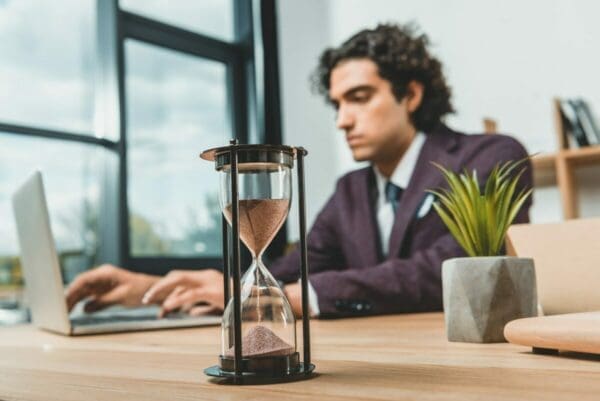 Sand timer on desk with focused businessman in background