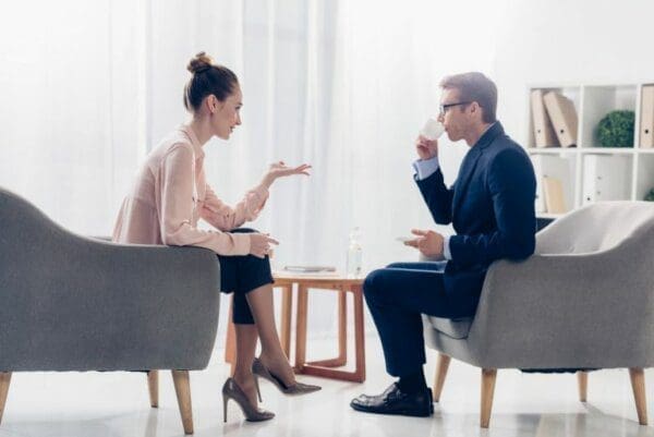 Two colleagues having coffee inthe office and asking questions