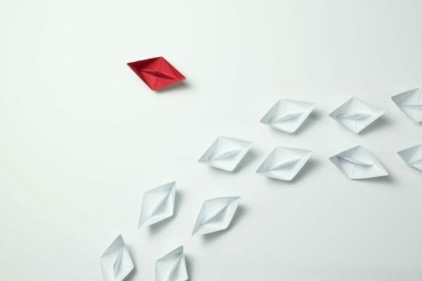 A row of origami white boats following a single red boat representing leadership