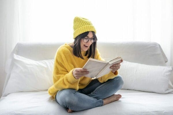 Girl in yellow reading on a white bed