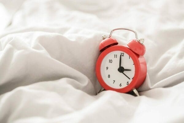 Red alarm clock laid on a crumpled duvet