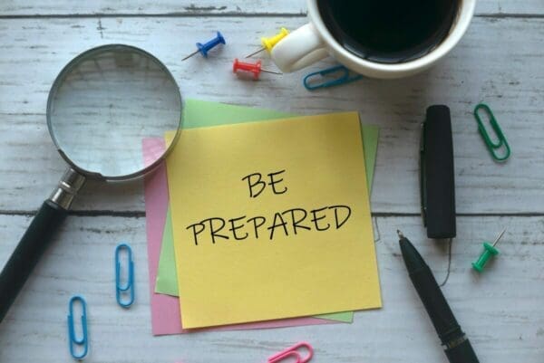 be prepared written on yellow note with magnifying glass, pen, and coffee mug