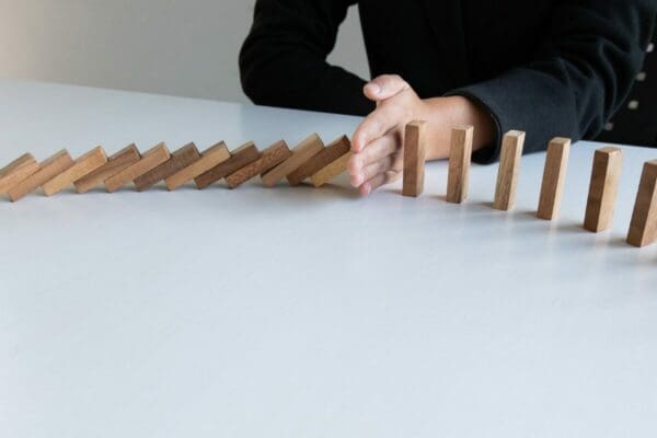 Building blocks falling in a line with a hand stopping them