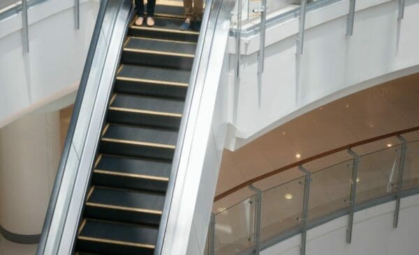 Close up of escalator heading down with two pairs of feet on the upper steps
