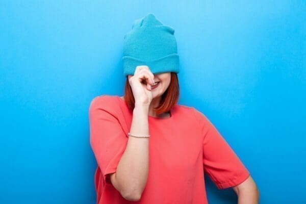 Smiling woman wearing blue hat hiding her face in front of blue background