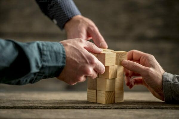 Hands of businessmen building a tower of wood blocks