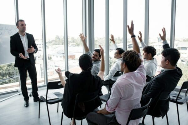 Male leader in a meeting room with colleagues raising their hands