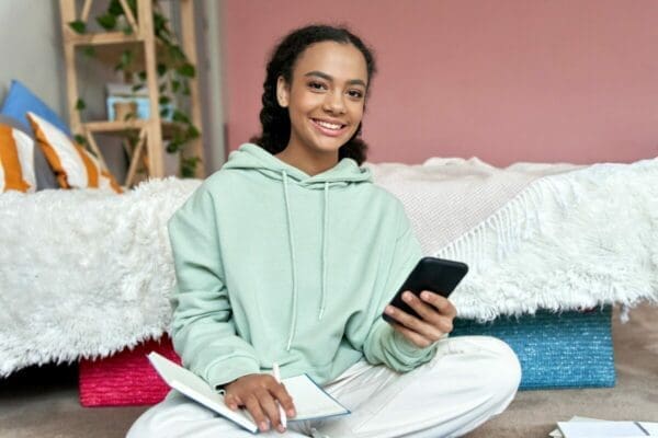 Girl on floor with notepad while using a revision app on her phone