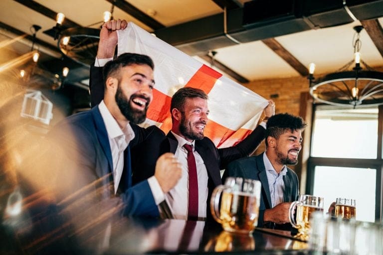 Men fans screaming and watching football on TV and drink beer in a pub