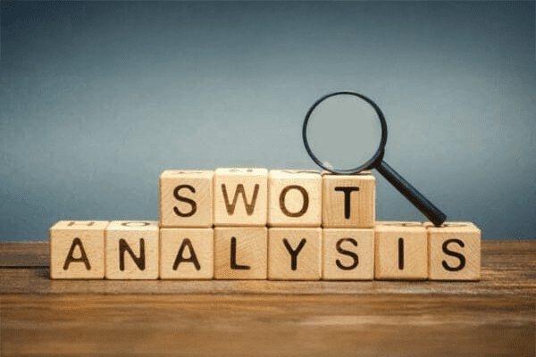 Wooden blocks spelling "SWOT ANALYSIS" with a magnifying glass resting on top, set against a blue background.