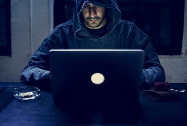 Hacker wearing a hood in the dark while working on a laptop doing cyber crime