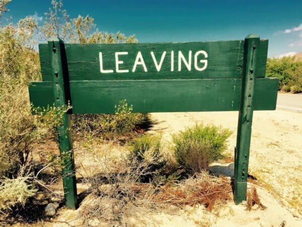 Green wooden sign with Leaving on it in white letters