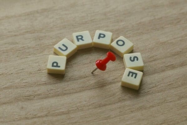 Purpose spelled with word scramble cubes on wooden table with red tack in the middle
