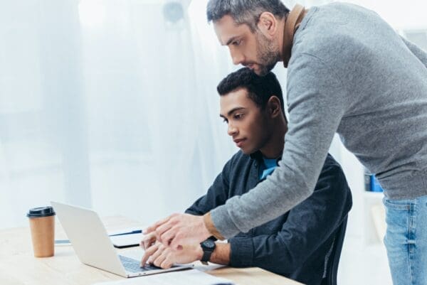 coach helping a young colleague working with a laptop in an office