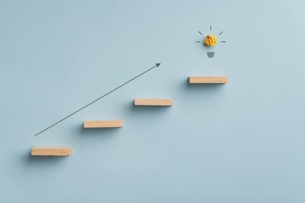 Wooden steps with arrow upwards pointing to a lightbulb