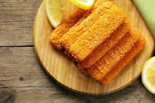 Pile of fish fingers on a wooden board garnished with lemon