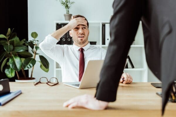 scared businessman with laptop looking at angry boss in office