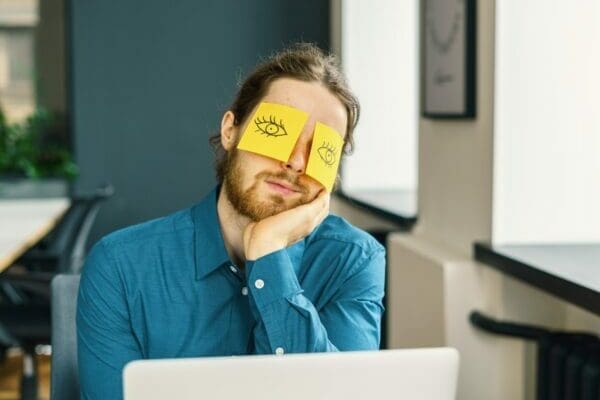 Problem employee with eye drawings on a yellow sticky note over his eyes is funny