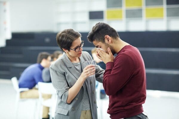 Female coworker comforting a man experiencing trauma and giving him water