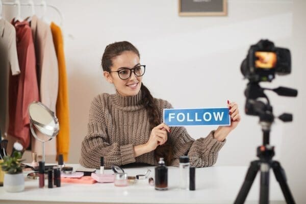 Social Media Influencer holding up a blue follow sign in front of a camera