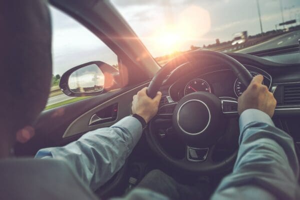 Inside view of a car with two hands on the steering wheel driving on a highway