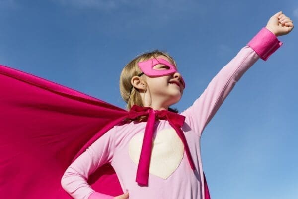 Little girl in a pink cape doing a superhero pose