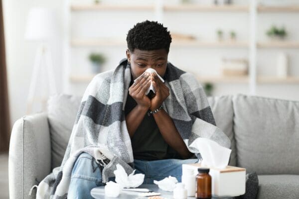 Man sitting on sofa sneezing into a tissue from poor health