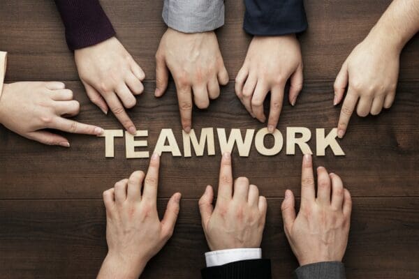 Teamwork letters on table with hands pointing to it. 