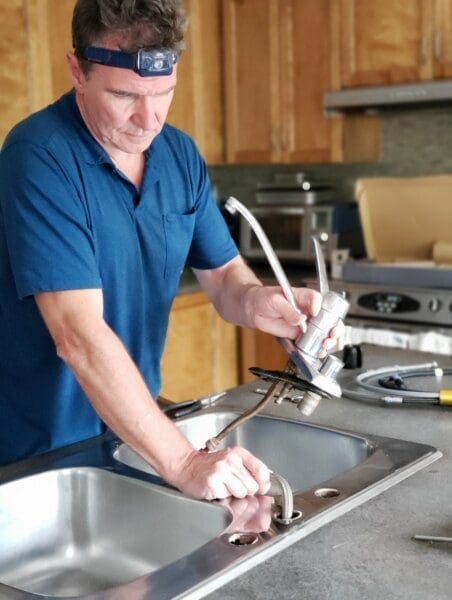 plumbing Handyman in a blue shirt with a forehead light is repairing a kitchen sink