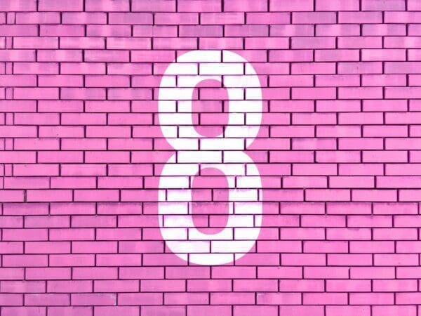 White number eight painted on a pink brick wall