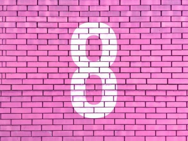 White number eight painted on a bright pink brick wall