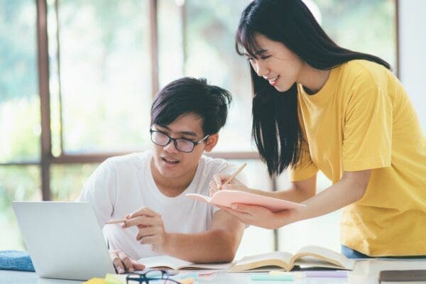 Two students learning from a laptop and books