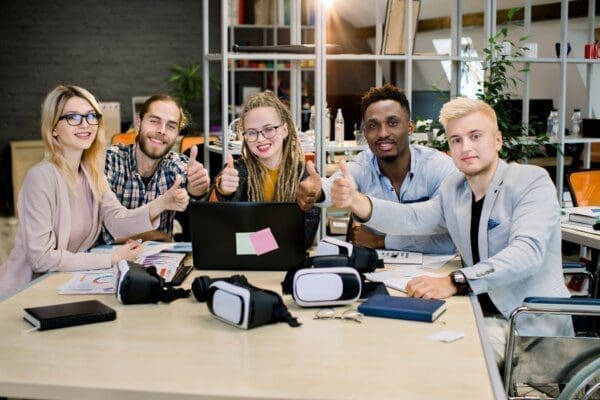 Team seated at a table with their thumbs up 