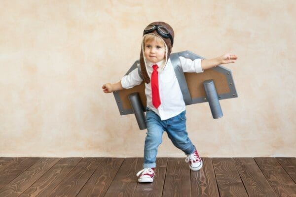 Little boy wears aeroplane wings and a flying hat as he imagines a pilot