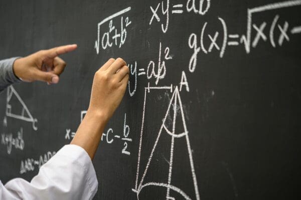 Hand writing formulas in white chalk on a black board.