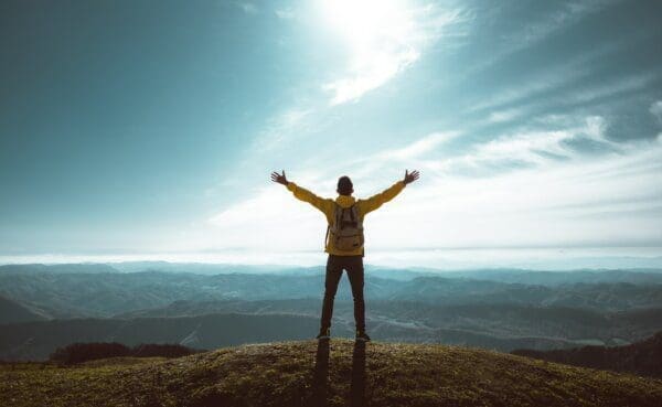 Hiker with stretched out arms standing on the top of the mountain - starting at the top