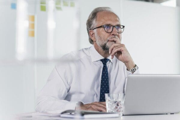Thinking businessman entp Mature businessman with laptop at desk in office thinking