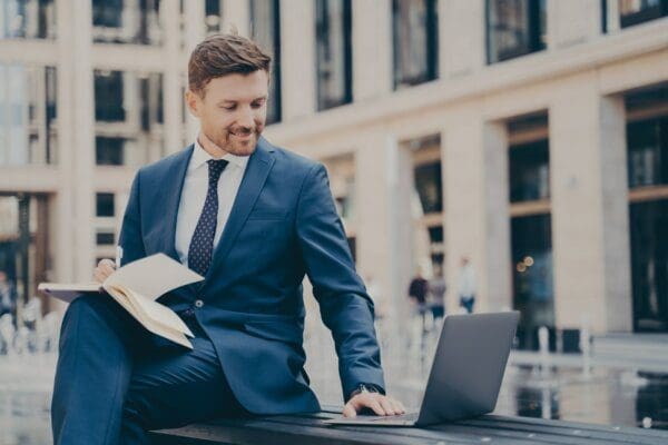 Businessman doing research Male employee doing research on a laptop while seated on a bench outdoors