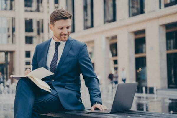 Male employee doing research on a laptop while seated on a bench outdoors