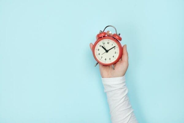 Red alarm clock in woman's hand on a blue background