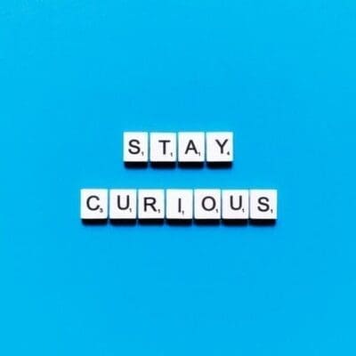 Stay curious written in scrabble tiles on a blue background