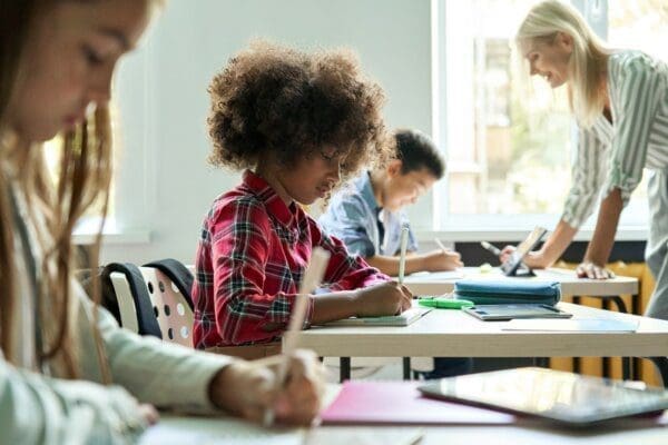 Diverse classmates doing task at lesson studying in classroom with teacher