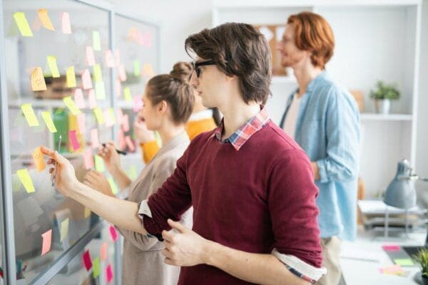 Three work employees organising post-it notes on glass screen