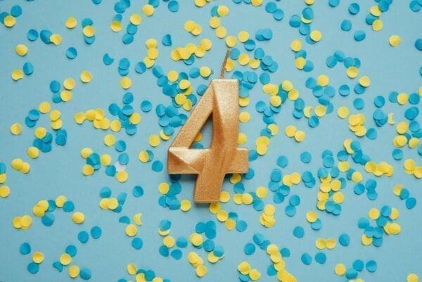 Number 4 four golden celebration birthday candle on yellow and blue confetti background