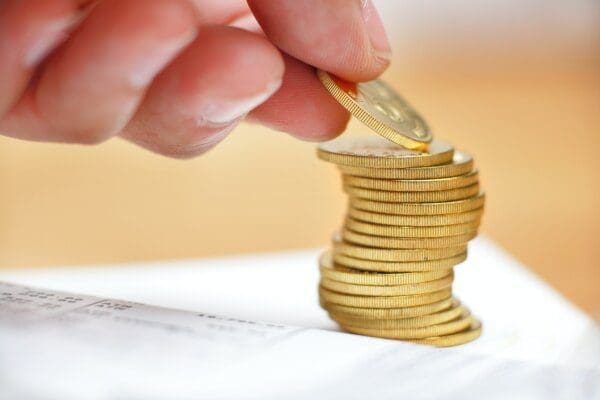 Hand putting single coin on a pile of gold coins