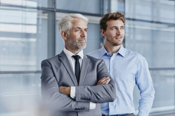 Confident business leader folding arms with employee behind