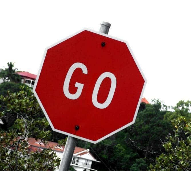 Sign Red GO sign with trees and houses in the background