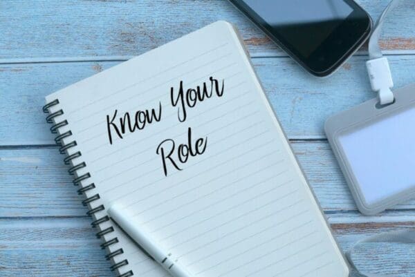 Know your role written on lined paper of a notebook next to a phone on a wooden table