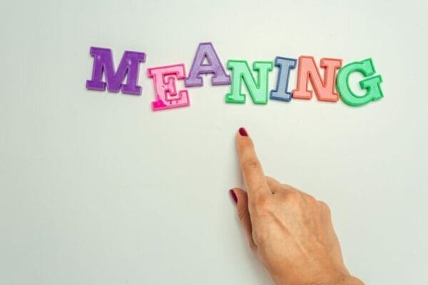 meaning meaning word spelt with colourful letter magnets with red nail painted index finger of female hand pointing to it