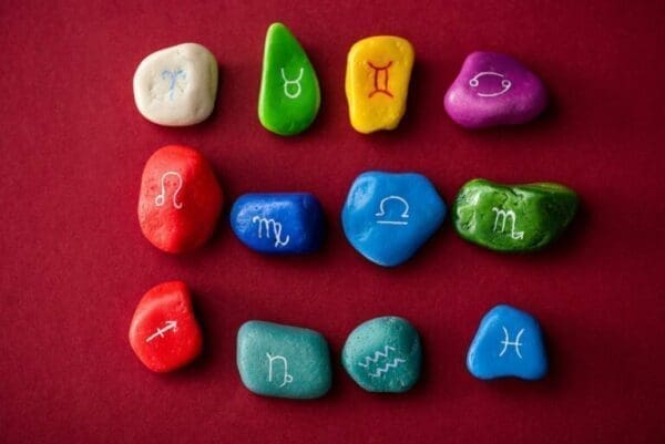 zodiac sun signs Top view of colorful stones with zodiac sun signs on red surface